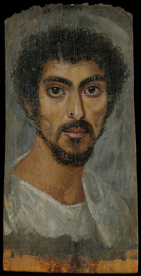 A portrait of a man with dark curly hair, facial hair, and large round eyes. He wears a white garmen