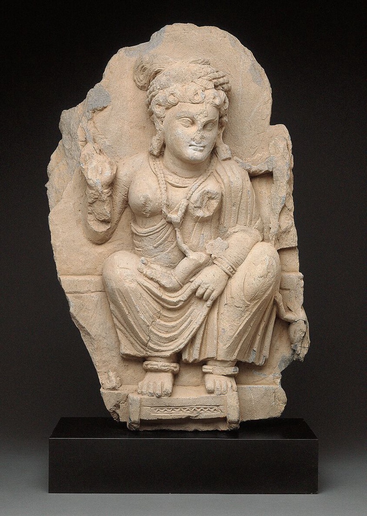 A Gandharan sculpture of the goddess, Hariti, seated and holding a child in her left arm. Her right