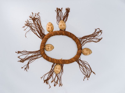 A thick, circular ring made out of natural fibers worn around a person’s neck. Five small carved hea