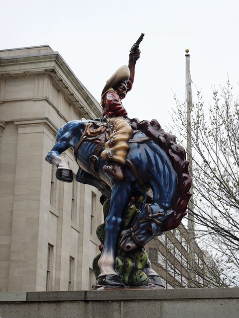 A sculpture of a blue horse bucking while a brown-skinned vaquero, or cowboy, proudly rides the hors