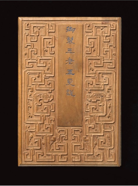 A wooden cover of an album that is decorated with a geometric pattern. A column in the center includ