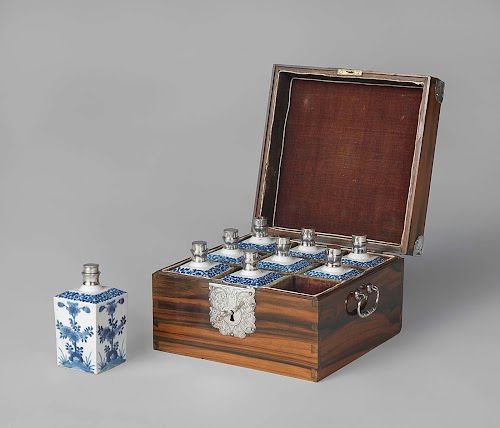 A set of nine porcelain bottles with blue decoration. Eight are placed in a gridded wooden box with 