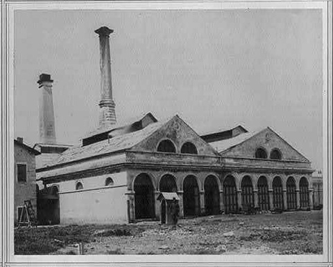 This black-and-white photographic image shows a large building with arched doorways, the early compe