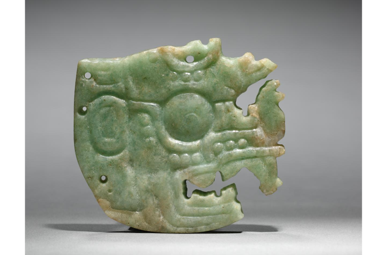 A Jadeite-albitite crown ornament carved in Maya style. The ornament features a deity in profile wit