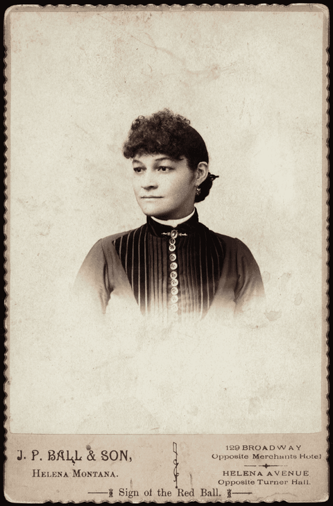 Head and shoulders portrait of an unidentified African American woman with brooch above buttoned shi