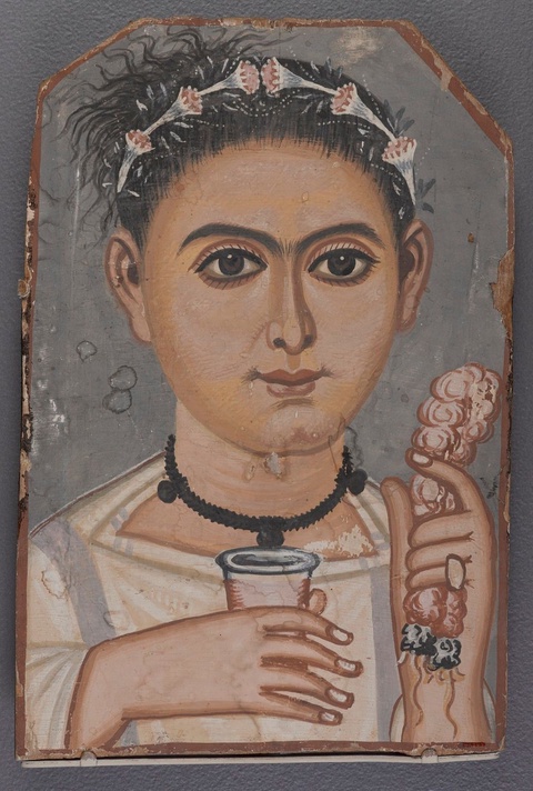 A portrait of a boy who is holding an object in each hand. His black hair is gathered in an updo and