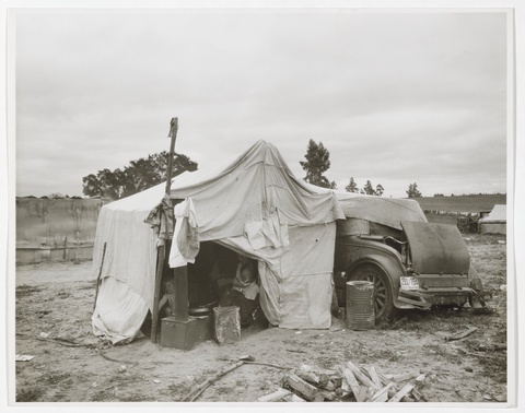 A black and white photograph depicts a temporary shelter made of sewn-together tarps propped up by p