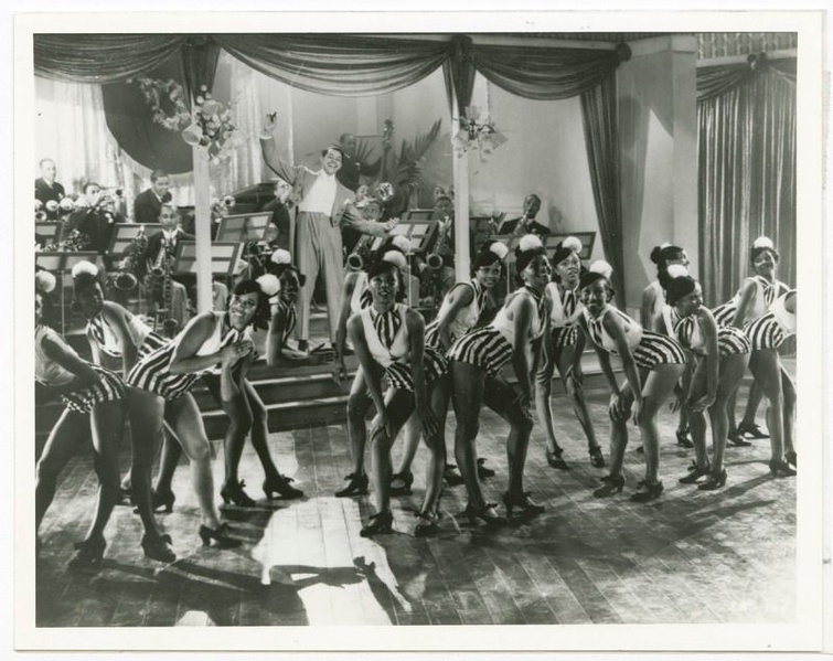 A black and white photograph of Cab Calloway with his dancers at the Cotton Club. Calloway stands in