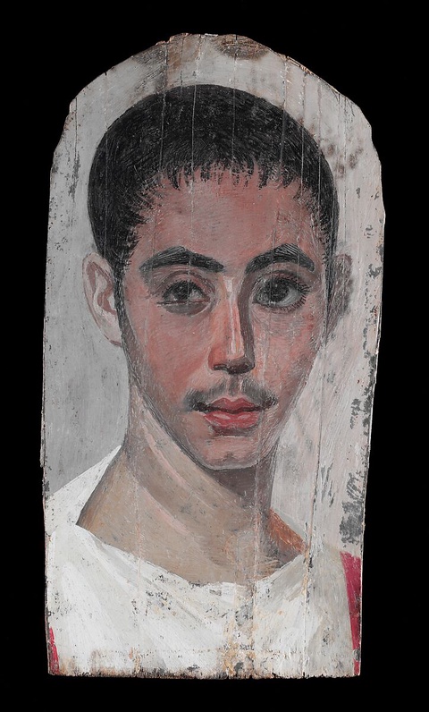 A portrait of a young man with hints of facial hair on his upper lip and jawline. He appears to have
