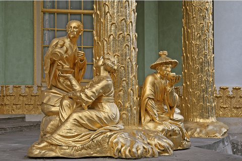 In view are three gilded chinoiserie statues holding parasols and instruments, and gilded columns in